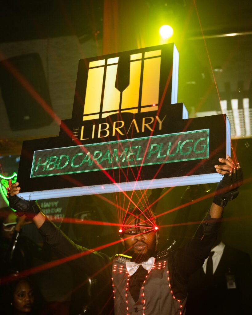 A male bartender at The Library Lagos lighting up a display board that reads “Happy Birthday Caramel” during the birthday celebration of Nigerian influencer Caramel Plug